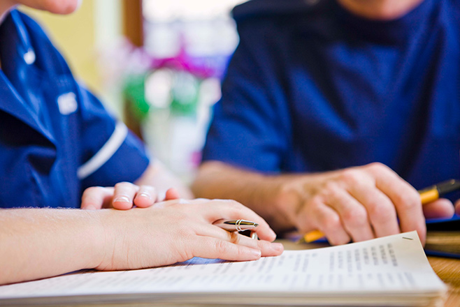 Two nurses sat at a table with a notepad and pen