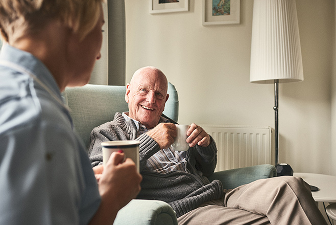 An elderly man drinking tea with a nurse