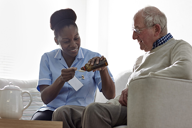 A nurse pouring medicine for an elderly man