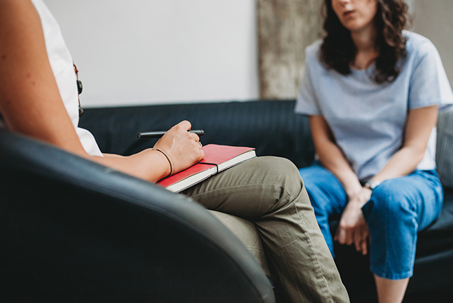 A woman on a couch talking to a person with a notebook